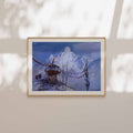 Framed artwork of a snowy landscape with a windmill on a beige wall.